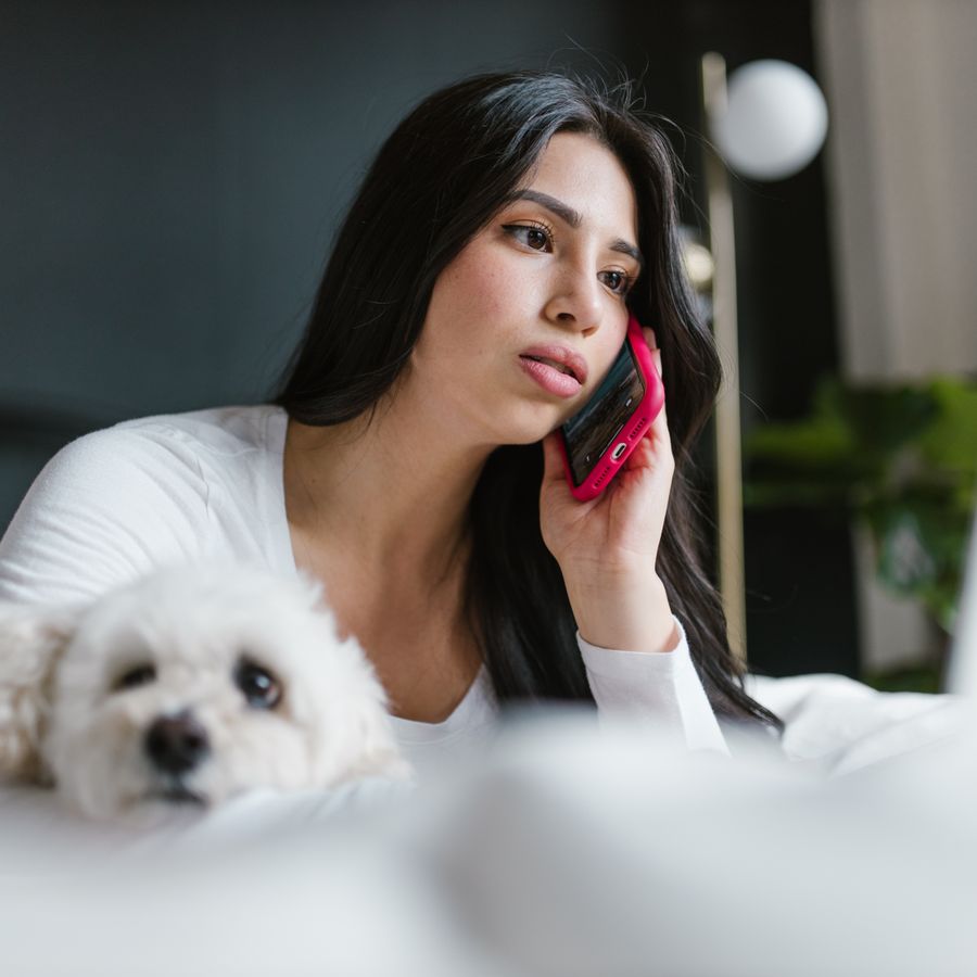 Woman on a phone call with her small white dog resting beside her